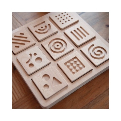 Peças quadradas de madeira clara com padrões em relevo em moldura quadrada de madeira.