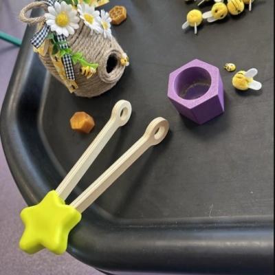 Casa de abelha decorativa, pinças de madeira com pontas amarelas e miniaturas de abelhas sobre mesa preta