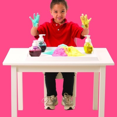 Criança com mãos cobertas de slime azul e amarelo sobre mesa branca com slimes coloridos