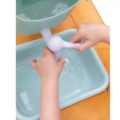 Dispositivo plástico lilás com alavanca sendo manipulado por mãos infantis sobre recipiente azul claro