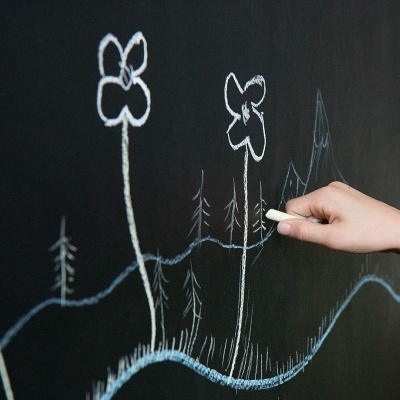 Desenho de flores com giz branco e azul num quadro negro, com uma mão desenhando