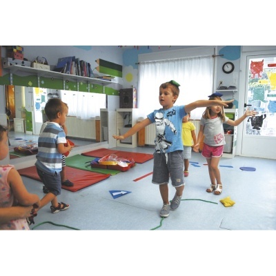 Crianças brincando numa sala de aula colorida com tapetes vermelhos e decoração educativa