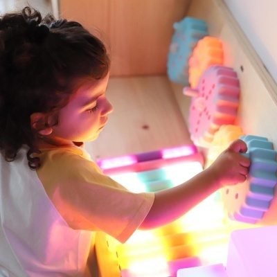 Criança a brincar com engrenagens plásticas coloridas numa parede de madeira