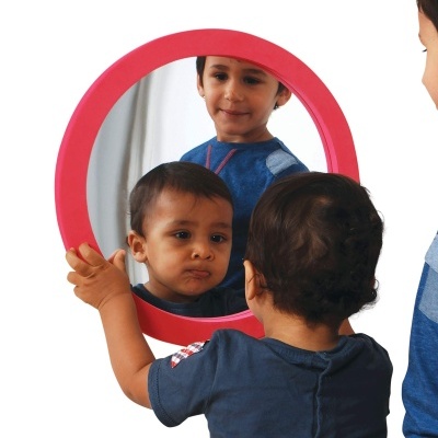 Criança segurando espelho redondo vermelho que reflete outra criança