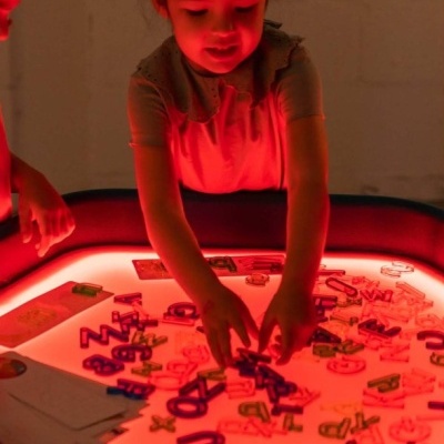 Criança a brincar com letras coloridas numa mesa iluminada