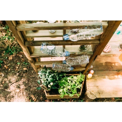 Estante de madeira com garrafas penduradas e plantas verdes ao ar livre