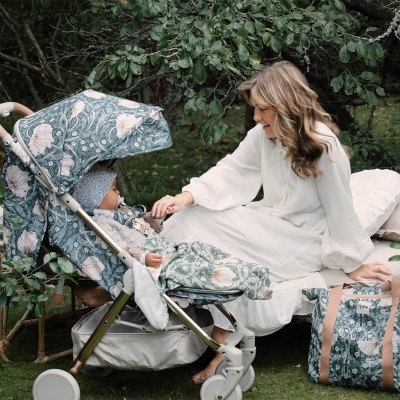 Carrinho de bebé estampado floral verde e branco com saco igual, mulher sentada na manta branca a sorrir para bebé