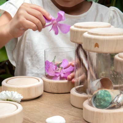 Frascos decorativos transparentes com bases e tampas de madeira clara e flores roxas