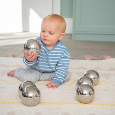 Bebé segurando bola metálica prateada sentado em tapete com bolas metálicas
