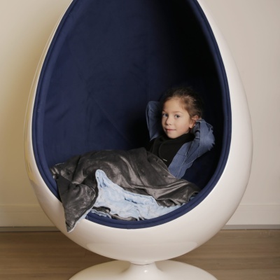 Poltrona egg chair branca com interior azul e criança sentada coberta por cobertor