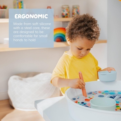 Criança a brincar com tigelas e colher numa mesa branca com jogos coloridos