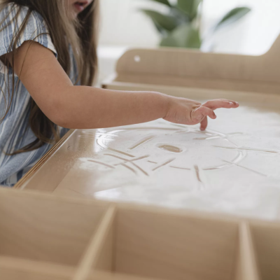 Criança a desenhar com o dedo num tabuleiro de madeira com pó branco