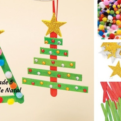 Dois enfeites de Natal verdes feitos com paus de gelado decorados com pompons coloridos e adesivos brilhantes, rodeados por materiais para artesanato