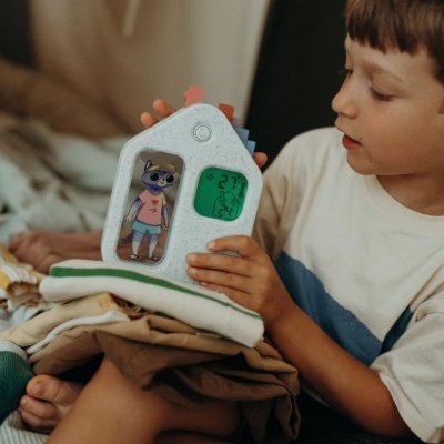 Dispositivo eletrônico em forma de casa com visor digital e figura de gato, nas mãos de uma criança.