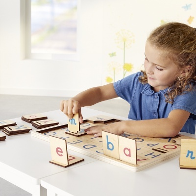 Menina a jogar jogo educativo de letras de madeira numa mesa branca.