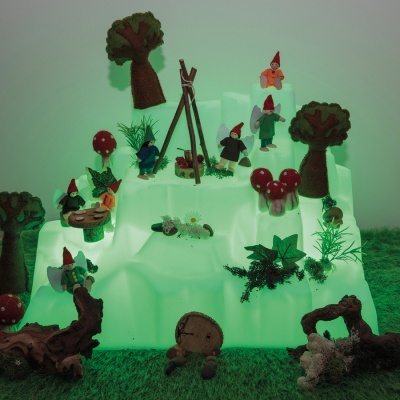 Miniaturas de gnomos, cogumelos e árvores em cenário iluminado verde sobre relva sintética