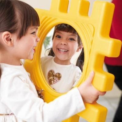 Criança sorridente olhando para um espelho oval amarelo