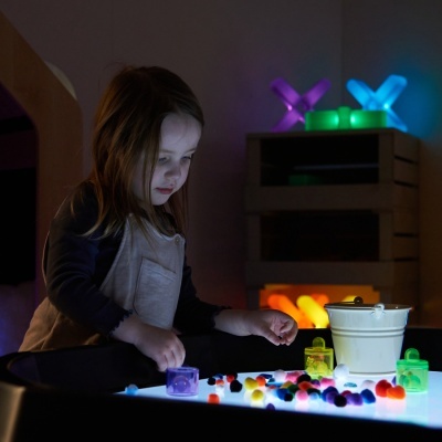 Criança a brincar com pompons coloridos numa mesa iluminada em ambiente interior