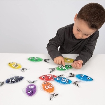 Menino a brincar com peixes de madeira coloridos numerados numa mesa branca