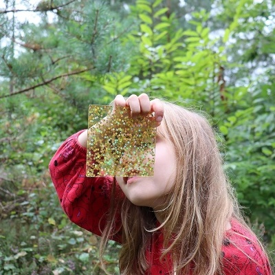 Jovem segurando pedaço quadrado transparente com pontos dourados em ambiente natural