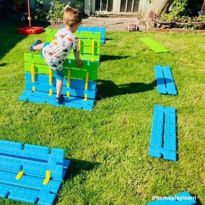 Criança no relvado a brincar com peças de plástico azul, verde e amarelas
