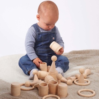 Bebé com jardineira azul a brincar com brinquedos de madeira no tapete