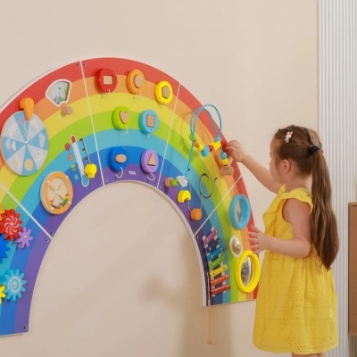 Painel de atividades infantil colorido em forma de arco-íris na parede com criança brincando