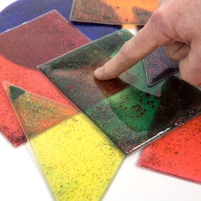 Peças de vidro colorido brilhante em várias formas geométricas com dedo a tocar uma peça verde.