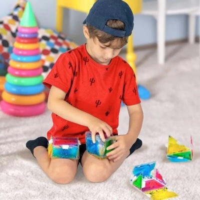 Criança com t-shirt vermelha e boné azul a brincar com blocos coloridos transparentes no chão.