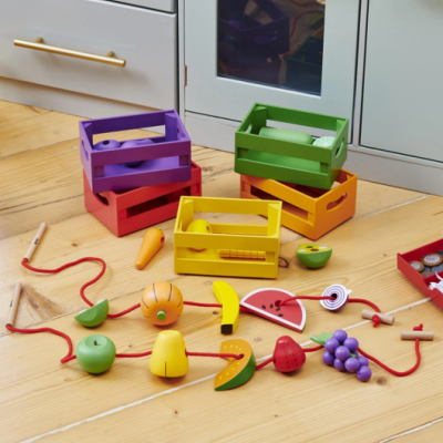 Brinquedos de madeira coloridos de frutas e legumes com caixas coloridas sobre chão de madeira clara