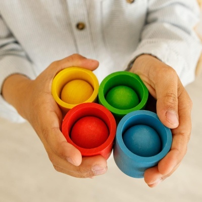 Mãos seguram quatro copos de madeira coloridos com bolas da mesma cor