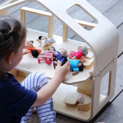 Criança a brincar com casa de bonecas em madeira clara e bonecos de tecido colorido
