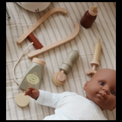 Boneca bebé castanha com acessórios médicos de brinquedo em tons neutros sobre tecido riscado