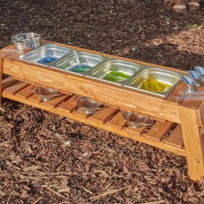 Mesa de madeira com cubas de metal contendo líquidos coloridos e acessórios em ambiente exterior