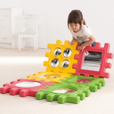 Peças de brinquedo coloridas com espelhos e criança a brincar numa sala clara