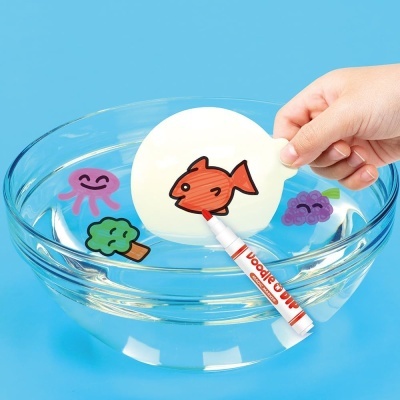Disco branco flutuante com peixe desenhado numa tigela de vidro cheia de água, ao lado de figuras coloridas, fundo azul