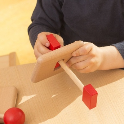 Brinquedo de madeira com formas coloridas em vermelho e madeira natural em mãos de criança