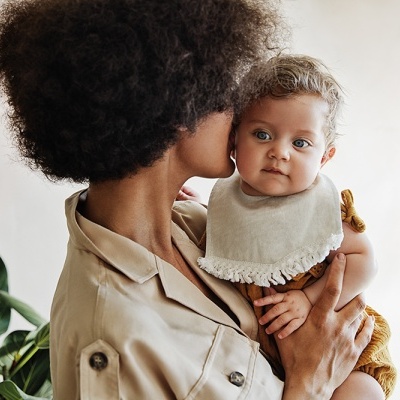 Mulher segurando bebé com babete em fundo neutro e planta