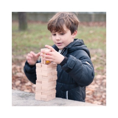 Menino a jogar jogo de blocos de madeira ao ar livre com casaco azul