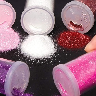 cinco frascos de glitter colorido sobre superfície preta, um frasco é segurado