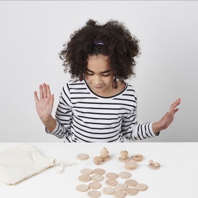 Peças de madeira claras espalhadas numa mesa branca e criança com camisa às riscas pretas e brancas ao fundo.