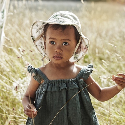 Criança pequena vestindo vestido verde-azulado e chapéu branco em campo