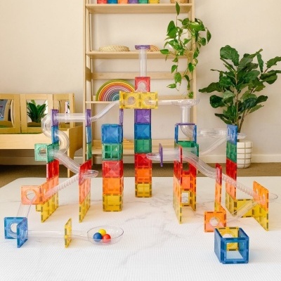 Estrutura de jogo de bolas colorida com tubos transparentes montada em sala com planta e estante ao fundo