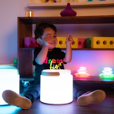 Criança com t-shirt colorida sentada junto de candeeiros luminosos e blocos coloridos