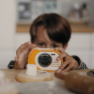 Criança com câmara fotográfica amarela e branca a tirar fotografia numa cozinha
