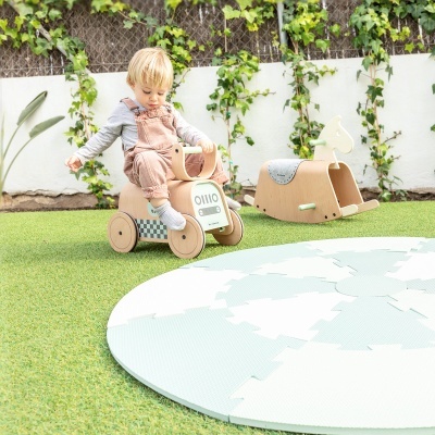 Criança a montar brinquedo de madeira num jardim com relva artificial