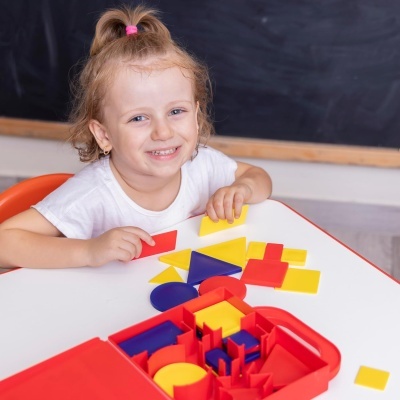 Criança a brincar com blocos geométricos coloridos em mesa branca