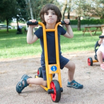 Criança num mini triciclo amarelo com rodas vermelhas e preto em parque