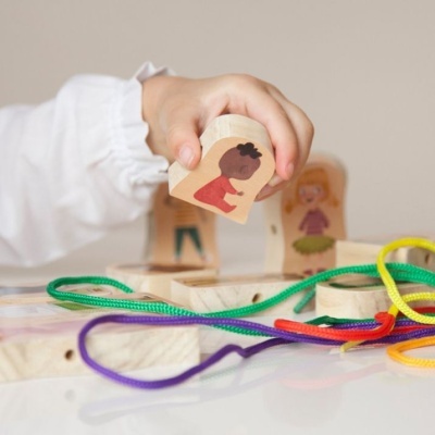 Peça de madeira em forma de coração com desenho de criança e cordões coloridos sobre mesa branca.