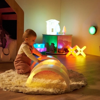 Criança a brincar com arco de luzes LED num quarto decorado com luzes coloridas.